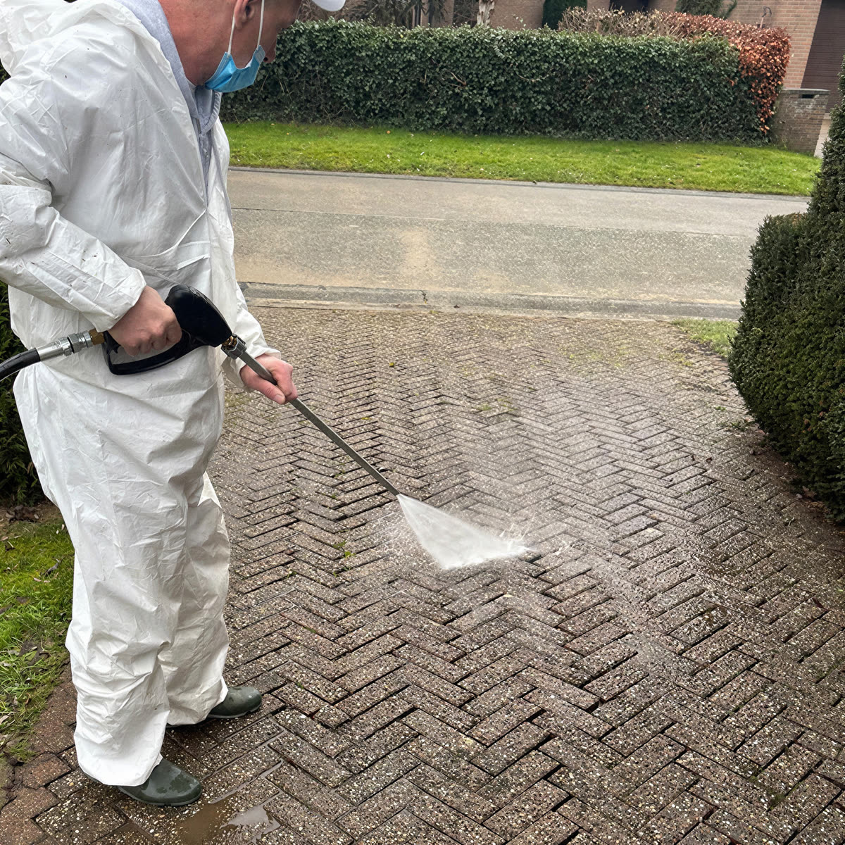 Oprit in klinkers tijdens de hogedrukreiniging, de lichte strook is al gereinigd.
