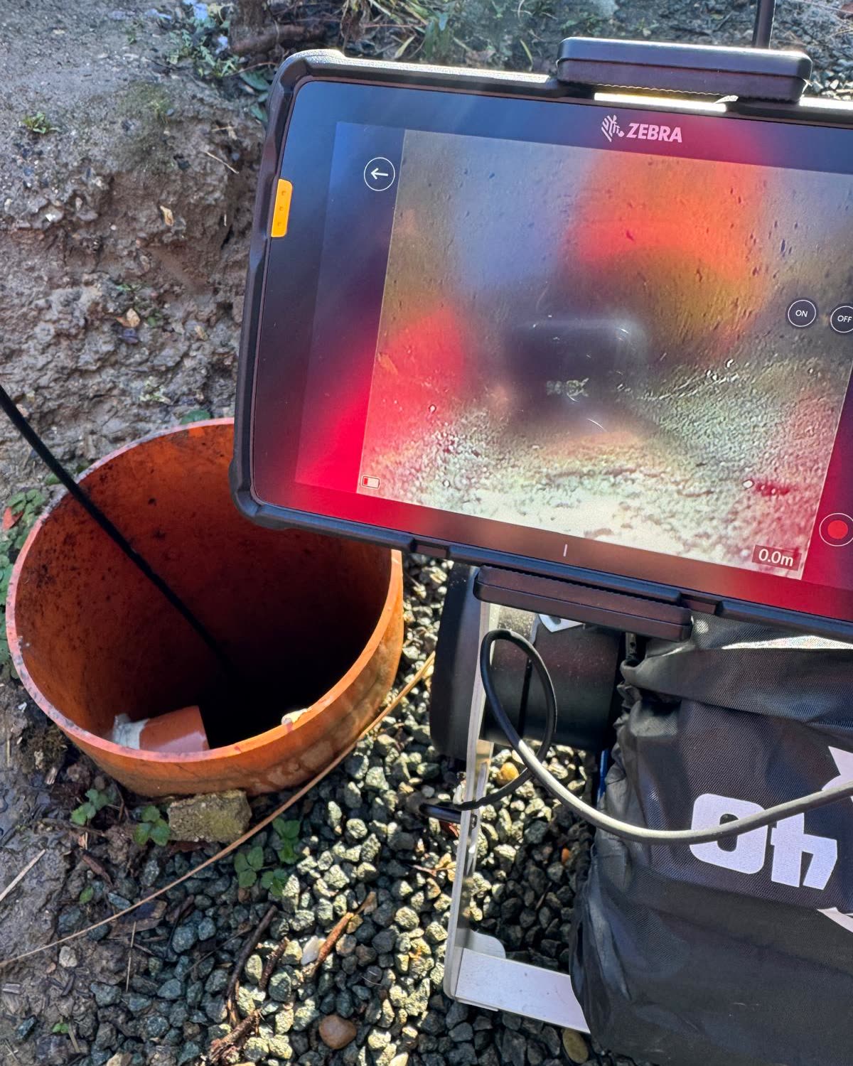 Tablet van de inspectiecamera boven een open put, de binnenkant van de buis op het scherm.