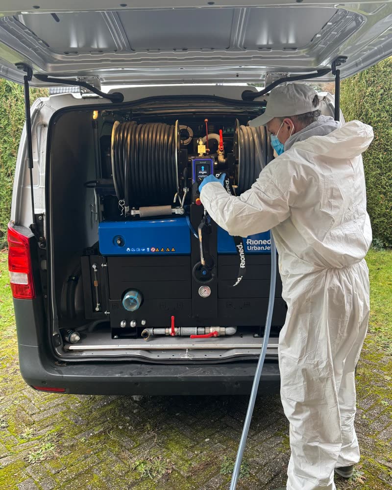 Technieker in beschermkledij bij de hogedrukmachine, achteraan in de bestelwagen.