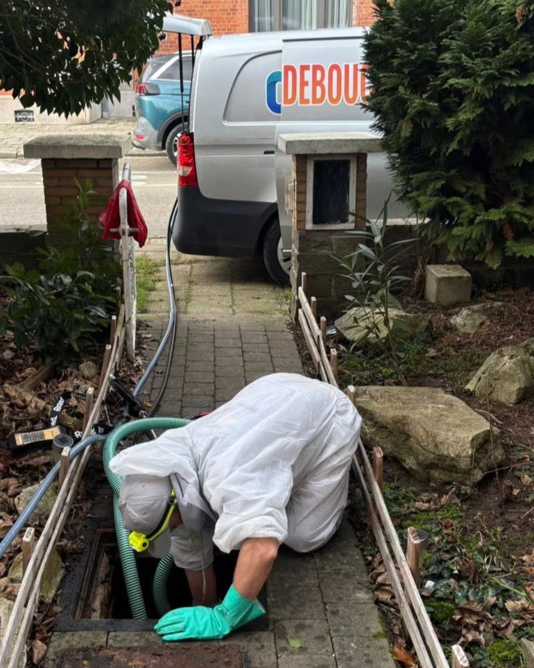 Technieker gebogen over een toezichtsput voor een woning, de bestelwagen staat op straat.