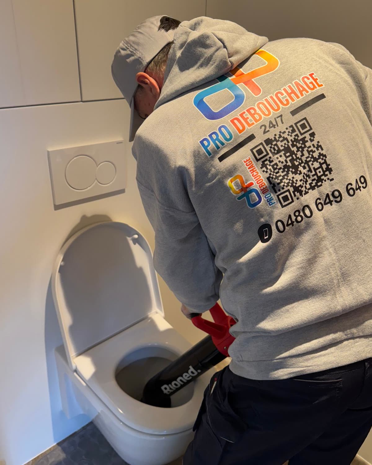 Technieker die een wc ontstopt met een Rioned veer, in Pro Débouchage kledij.